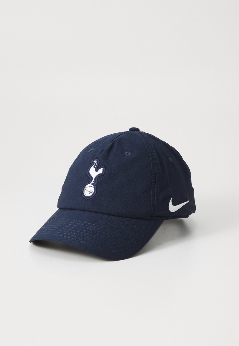 Mörkblå keps med rund skärm, prydd med en vit broderad logotyp och Nike swoosh. Tillverkad av slitstukt tyg med ventilationshål.