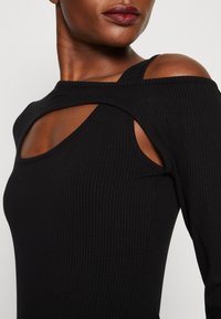 Top lungo a maniche nere a coste con design con spalle scoperte e silhouette aderente. Il materiale morbido e elasticizzato mette in evidenza i contorni del corpo.