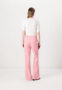 Jasnoróżowe, dopasowane spodnie z rozszerzanymi nogawkami i tylnymi kieszeniami, zestawione z prostą, białą koszulą z krótkim rękawem. Gładka faktura.