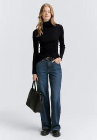 Un col roulé noir à côtes, un jean bleu à jambes larges, une ceinture noire et un grand sac à main noir. Texture lisse avec une silhouette ajustée et un design décontracté.