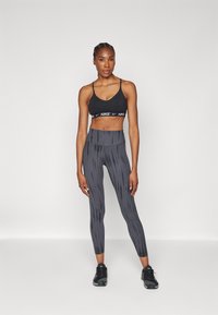 Sujeción deportiva negra con el logo de Nike, combinada con mallas grises de cintura alta que presentan un patrón de rayas verticales y zapatillas deportivas negras.