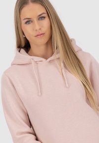 Felpa rosa chiaro con una texture morbida, cordini e un fit rilassato. Il materiale sembra comodo, adatto per un abbigliamento casual.
