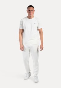 Hvid bomulds t-shirt med korte ærmer, rund hals, diskret logo detalje på brystet, parret med hvide sweatpants og sneakers.