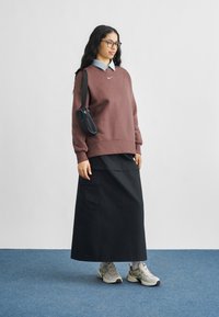 Μπορντό φούτερ με στρογγυλή λαιμόκοψη, από μέσα φοράει ανοιχτό μπλε πουκάμισο με γιακά. Μαύρη μακριά φούστα, μπεζ αθλητικά παπούτσια και μικρή μαύρη τσάντα ώμου.