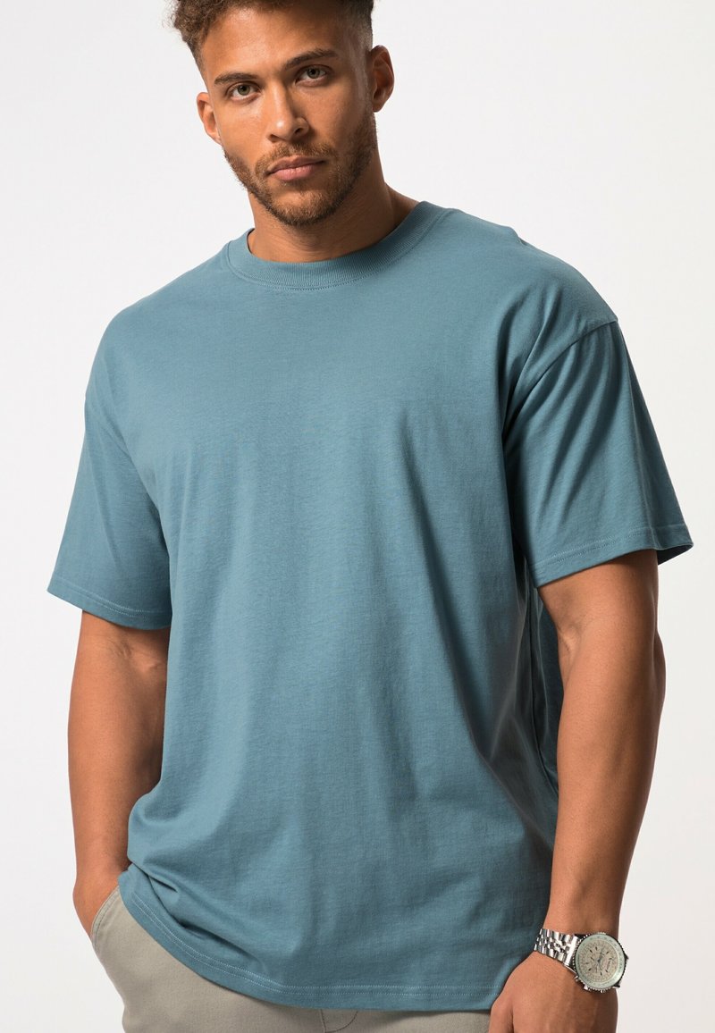 Heren T-shirt met korte mouwen in een gedempte blauwe kleur, gemaakt van zachte katoen, met een ronde hals en een relaxte pasvorm. Metallic horloge om de pols.