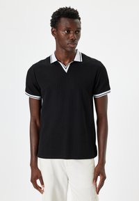 Svart polo skjorta med ribbad textur, prydd med en vit V-ringning och kontrasterande vit kant på de korta ärmarna.