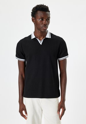 Camisa polo negra con textura acanalada, con un cuello en V blanco y un ribete blanco que contrasta en las mangas cortas.