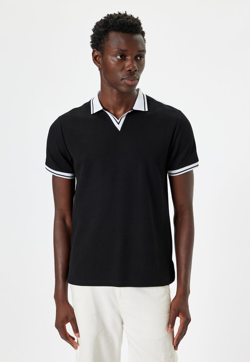 Svart polo skjorta med ribbad textur, prydd med en vit V-ringning och kontrasterande vit kant på de korta ärmarna.