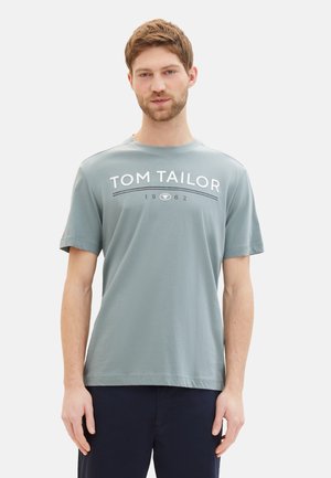 Camiseta de algodón gris con cuello redondo y mangas cortas, con "TOM TAILOR 1962" impreso en blanco contrastante a lo largo del pecho.