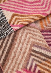 Tessuto morbido intrecciato con motivi geometrici a zigzag in tonalità di rosa, marrone, beige e arancione, con bordi frangiati.