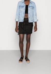 Light blue denim jacket over a black crop top, paired with a black polka dot skirt featuring a twist design and layered texture. Black platform sandals.