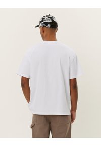 Weißes Baumwoll-T-Shirt mit kurzen Ärmeln und geradem Schnitt, kombiniert mit einer gemusterten Schwarz-Weiß-Kappe mit gebogenem Schirm.