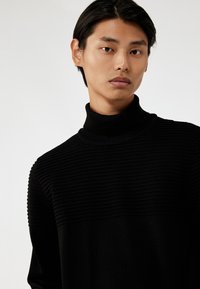 Jersey de cuello alto negro con un diseño de canalé texturizado en la mitad superior, material suave en la parte inferior, silueta ajustada y cuello acanalado.