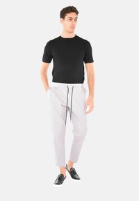 Maglione nero a coste a maniche corte, pantaloni grigi chiari a gamba stretta con cordino, e scarpe nere slip-on con suole bianche.