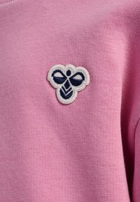 Jasnoróżowa bawełniana tkanina z granatowym haftowanym emblematem pszczoły. Tekstylia są gładkie i mają drobną teksturę splotu.