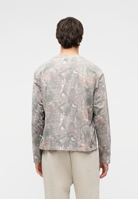 Πουκάμισο με μακριά μανίκια σε απαλό γκρι χρώμα με καμουφλάζ σχέδιο. Μαλακό ύφασμα με άνετη εφαρμογή και στρογγυλή λαιμόκοψη. Μινιμαλιστικός σχεδιασμός.