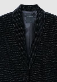 Blazer in velluto nero con superficie testurizzata, dotato di revers, chiusura con un bottone e fodera interna. L'etichetta riporta "CALLIOPE."