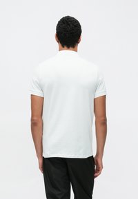 Fehér, rövid ujjú polóing szabványos gallérral, puha tapintású anyagból, egyenes szabású és felhajtott ujjú, sötét nadrággal párosítva.