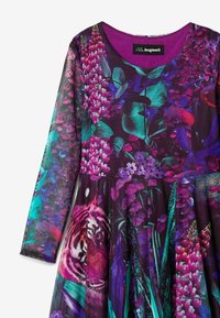 Langärmliges Kleid mit einer lebhaften lila Basis, verziert mit Blumen- und Tigerdruck in Tönen von Türkis, Pink und Grün. Strukturierter Stoff mit einem fließenden Rock.