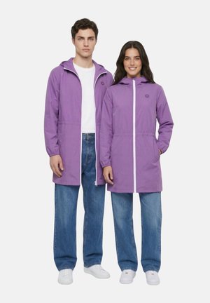 Jeune homme et femme portant des vestes à capuche violettes assorties, des jeans bleus et des baskets blanches, debout côte à côte sur un fond blanc.