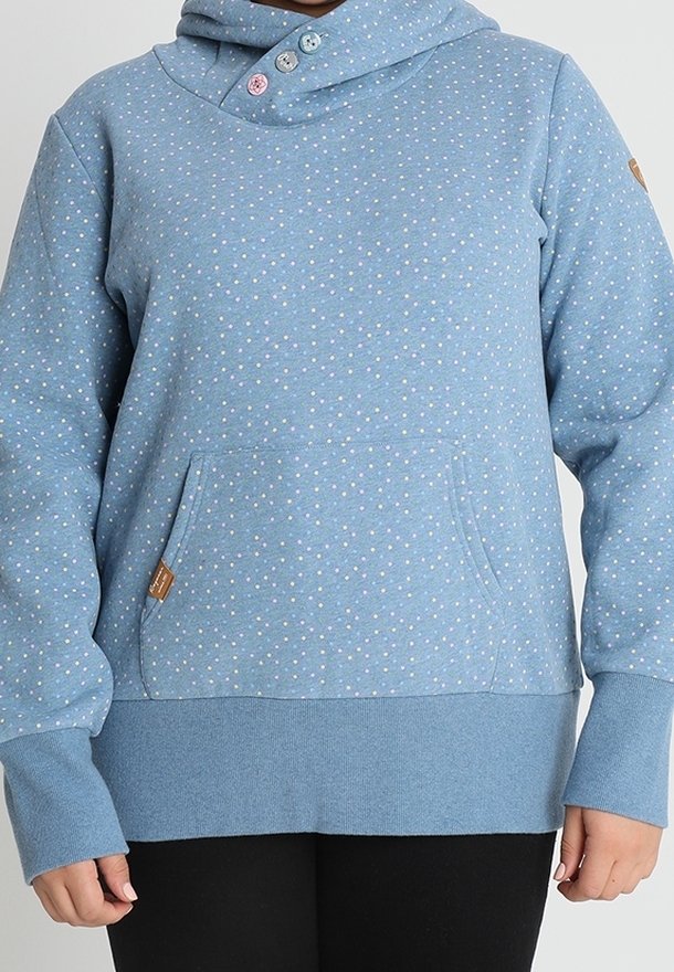 Mujer vistiendo un hoodie de color azul claro con pequeños lunares blancos y rosas, agujeros para el pulgar en los laterales y un bolsillo tipo canguro en la parte frontal.