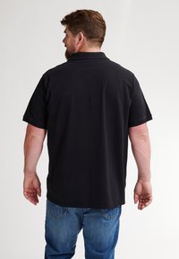 Musta poolopaita, valmistettu sileästä kankaasta, jossa on klassinen kaulus ja lyhyet hihat. Yhdistetty sinisiin farkkuihin. Näkyvät saumat ja ompeleet.