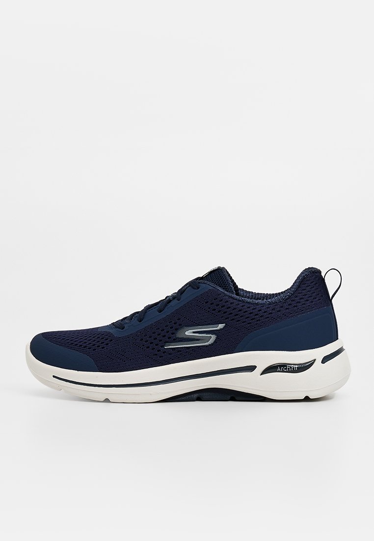 Zapatillas deportivas de color azul marino, fabricadas con una malla transpirable, que cuentan con una suela blanca y un logo plateado. Diseñadas con una puntera redondeada y un collar acolchado.