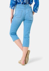 Pantaloni capri in denim azzurro chiaro con design aderente, vita media e lunghezza cropped. Presentano tasche posteriori e orlo sfilacciato.