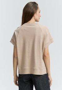 Sweat-shirt beige à manches courtes avec une coupe décontractée, doté d'un col rond et d'un ourlet côtelé, porté sur un jean sombre. Texture douce et design décontracté.