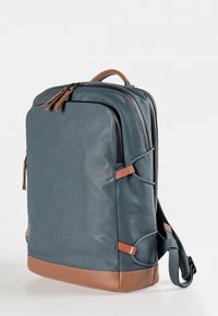 Zaino in pelle blu scuro con accenti marroni. Presenta una chiusura superiore con zip, texture liscia e un design minimalista con strap laterali per la regolazione.