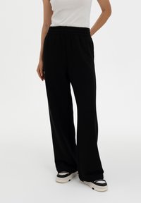 Black wide-leg pants made of soft fabric with an elastic waistband. Paired with black and white sneakers for a contrasting look.