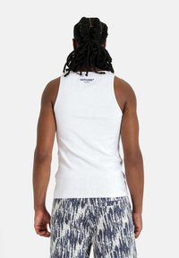 Top in cotone bianco con texture a coste, con un logo blu sul retro. Abbinato a pantaloni corti a fantasia in blu navy e bianco.