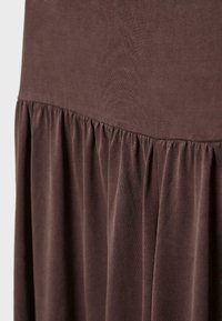 Tissu marron doux avec une couture froncée créant un effet volanté, montrant la texture et la chute du matériau du vêtement.