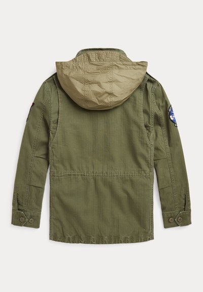 λαδί πράσινη ζακέτα με μπεζ κουκούλα, διαθέτει μία ετικέτα στο δεξί μανίκι και κουμπωτές μανσέτες. Το υλικό φαίνεται ανθεκτικό με λείο υφή.