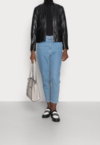 Black leather jacket with zipper, light blue high-waisted jeans, black and white shoes, and a beige handbag with double handles.