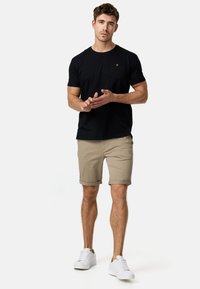 Schwarzes T-Shirt mit kurzen Ärmeln und einer Brusttasche, kombiniert mit beigen hochgekrempelten Shorts und weißen Sneakern. Lässig, moderner Schnitt.