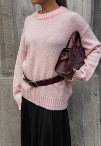 Rozā adīta džemperis ar ribotu apakšmalu, kombinēts ar tumšām piegriezuma svārkiem un mazu bordo ādas somiņu un atbilstošu jostu.