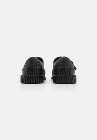 Czarne buty na platformie z gładką cholewką, z wyraźną gumową podeszwą. Z tyłu znajduje się logotyp oraz pętla ułatwiająca zakładanie.