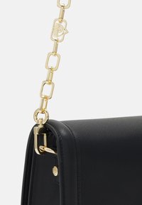 Svart läderhandväska med en texturerad yta, med ett guld kedjesnöre och en detaljerad guldmetallspänne.