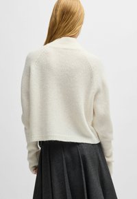 Weißer, verkürzter Pullover aus weichem, gestricktem Material mit gerippten Bündchen und Ausschnitt, kombiniert mit einem plissierten, dunkelgrauen Rock.