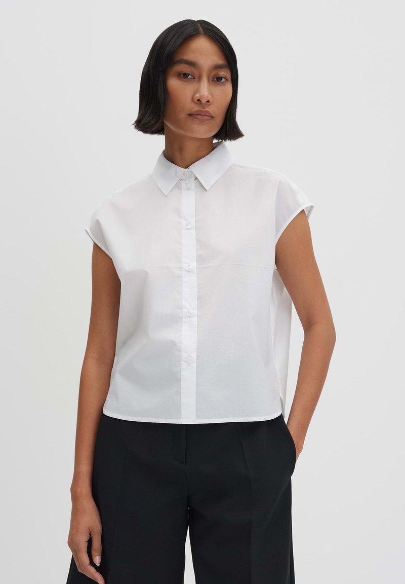 Camicia bianca a maniche corte con colletto, davanti con bottoni e orlo dritto, realizzata in un tessuto morbido e leggero.