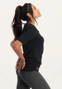 Svart kortärmad träningströja med figurnära design, mjuk textur och rynkad detalj vid nederkanten, tillsammans med mörkgråleggings.