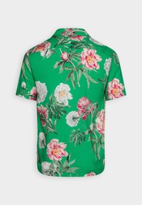 Camisetta a maniche corte con uno sfondo verde e grandi motivi floreali in rosa, bianco e pesca; tessuto morbido e design con colletto classico.