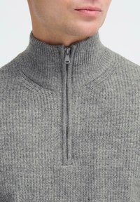Grijze zip-up trui met een hoge kraag, gekenmerkt door een ribbelstructuur en subtiele naden, waardoor een snug fit rond de nek en borst ontstaat.