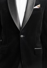 Zwarte fluwelen tuxedojack met satijnen revers, enkele knoopsluiting en een kleine patroon pocketvierkant. Heeft zijzakken met trim.