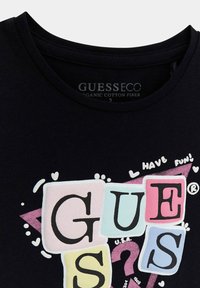 Camiseta de algodón orgánico negra con letras de bloques coloridas que deletrean "GUESS," con acentos gráficos como corazones y símbolos divertidos.