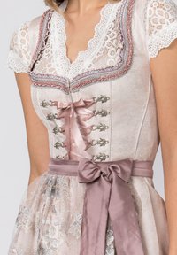 Hellrosa Dirndl mit Spitzenärmelchen, Spitzenrand und silbernen Akzenten. Verfügt über ein tailliertes Oberteil, dekorative Haken und eine Satinschleife in der Taille.