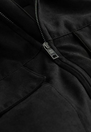 Schwarze Fleecejacke mit metallischem Reißverschluss, zwei Taschen und glatter Textur mit subtilen Nahtdetails.