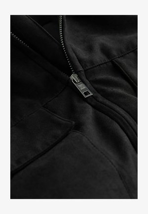 Giacca in pile nera con zip metallica, due tasche e texture liscia con dettagli di cucitura discreti.