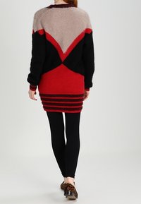 Maskerad klänning i svart, röd och beige med geometrisk design. Har ribbad textur och en figurnära nederdel. Bärs med svarta leggings.